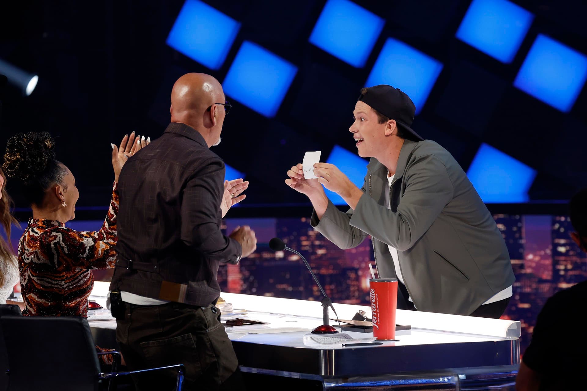 Geno revealing a card trick on stage as judges applaud during one of his live television performances